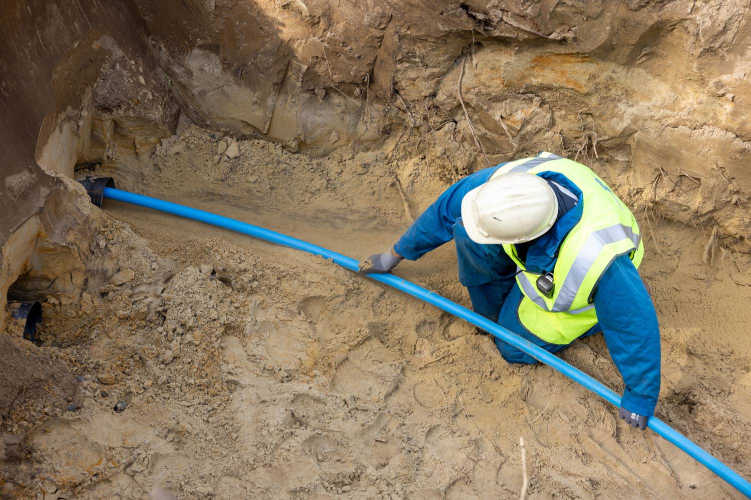 Monteur legt een blauwe HDPE-buis in een open sleuf