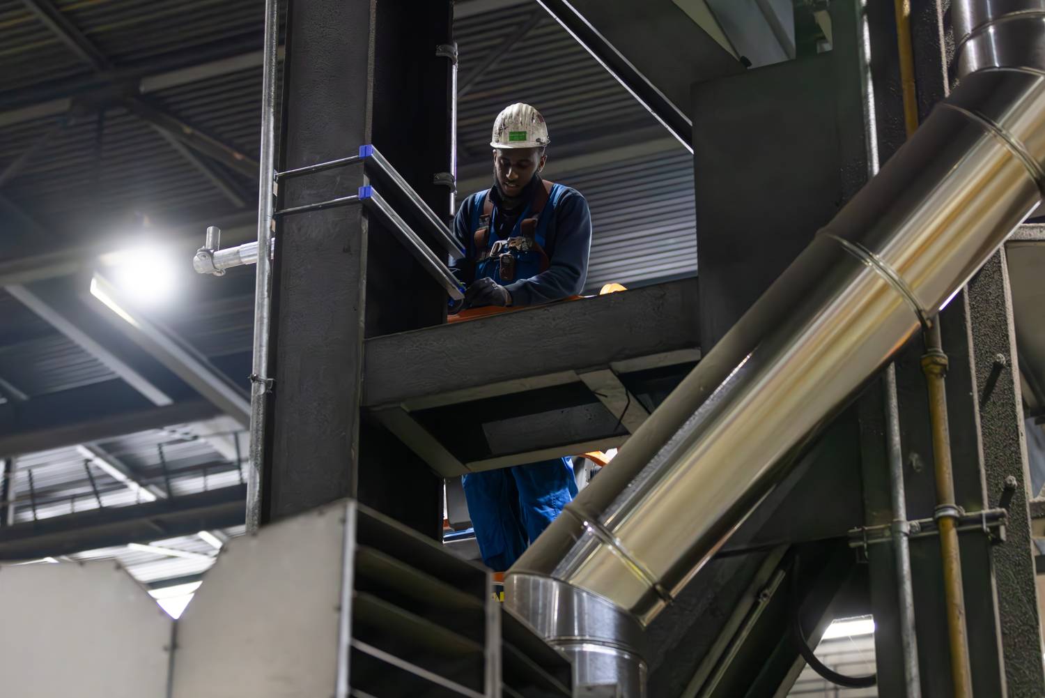 Monteur op een industriële installatie tussen leidingen en staalconstructie