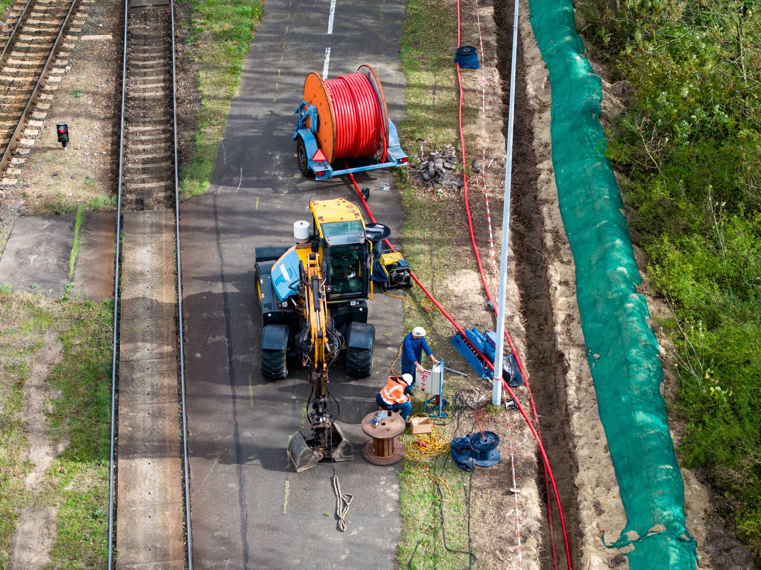 Kabelwerk langs een spoorlijn, met kraan en kabelhaspel, van boven gezien